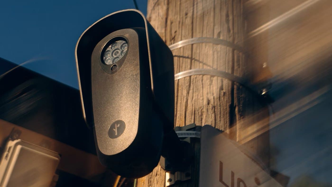 A Flock license plate reader strapped to a utility pole at dusk, beside a sign reading "License Plate Reader — Property of Seneca PD"